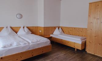 A simple room with two beds and an additional cot. The walls are made of wood, and the room feels cozy and bright.