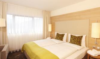 A modern hotel room with two beds and a warm, inviting color palette.  
Large windows provide plenty of daylight and a cozy atmosphere.