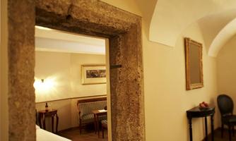 A cozy room with a stone arch and wooden floor. In the background, furniture and a bed are visible.