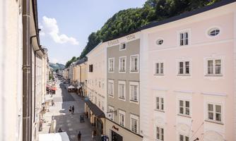 A quiet street view with historic buildings in soft colors. In the background, trees can be seen, and the sky is clear and blue.