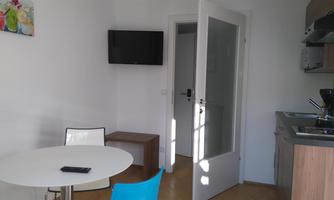 A modern kitchen with a round table and chairs. A television hangs on the wall, and a window lets in a lot of light.