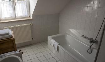 A bright bathroom with a bathtub, a sink, and folded towels. The walls are tiled in white, and a window provides daylight.