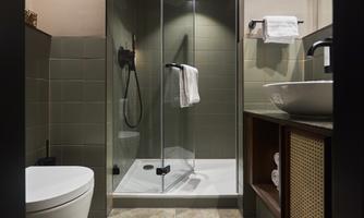 A modern bathroom with a glass shower and a stylish sink. The walls are painted in soft green tones and the decor is minimalist.