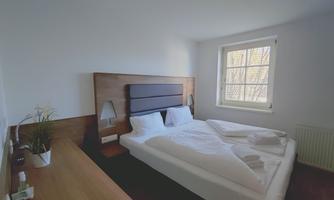 A bright bedroom with a large double bed and a wooden desk. Windows ensure plenty of daylight and a pleasant atmosphere.