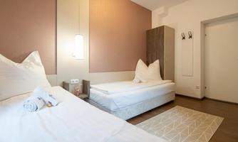 A modern room with two beds and a simple design. The walls are painted in soft colors, and there is a small rug on the floor.