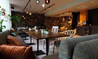 A modern café with cozy seating and plants. There are wooden panels and soft lighting that create an inviting atmosphere.