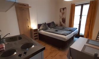 An elegant room with a double bed, table, and chairs. The kitchen is well-equipped, and large windows let in plenty of light.