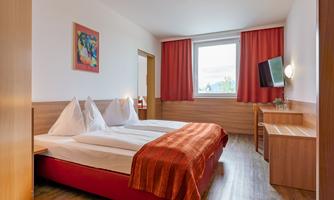 A cozy hotel room with two single beds and red curtains. A piece of art hangs on the wall, and the room features a television and a desk.