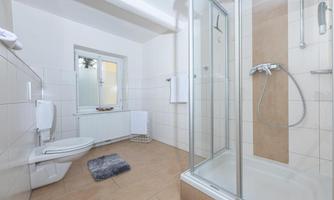 A modern bathroom with a shower and a toilet. Bright tiles and a large window create an open feeling.