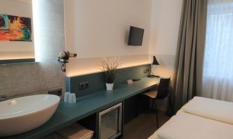 A modern hotel room with a minimalist design. It features a sink, a desk, and two single beds.