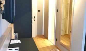 A modern room with a desk, television, and a large mirror. The walls are in neutral colors and the floor is made of light wood.