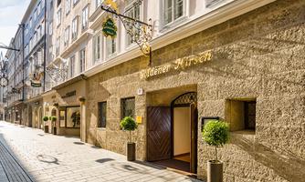 A charming building with the inscription "Golden Stag" on a quiet street. The facade is made of natural stone, and there are decorative plants at the entrance.