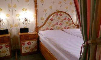A cozy bedroom with a bed and floral wallpaper. The nightstands are made of wood and have lamps on both sides.