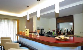 An elegant bar with a red counter and modern hanging lamps. In the background, drinks and snacks are placed on a shelf.
