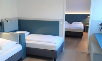 A modern room with two single beds and a minimalist design. There is a desk and soft lighting.