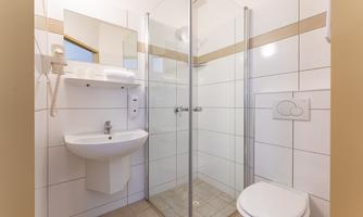 A modern bathroom with a glass shower, a sink, and a toilet. The walls are designed with light tiles.