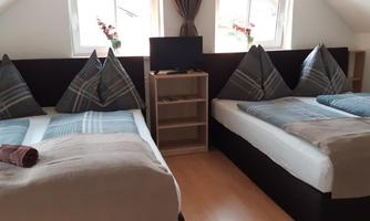 A cozy bedroom with two single beds and blue bedspreads. Next to the beds is a small wardrobe and a television.
