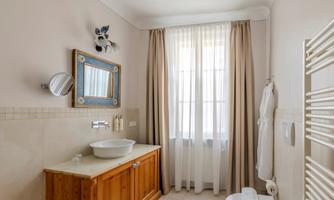 A modern bathroom with a wooden dresser and a sink. Large windows with curtains provide bright, natural light.