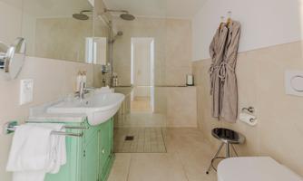 A modern bathroom with a green sink cabinet and a shower. The walls are brightly designed and there is a bathrobe as well as towels.