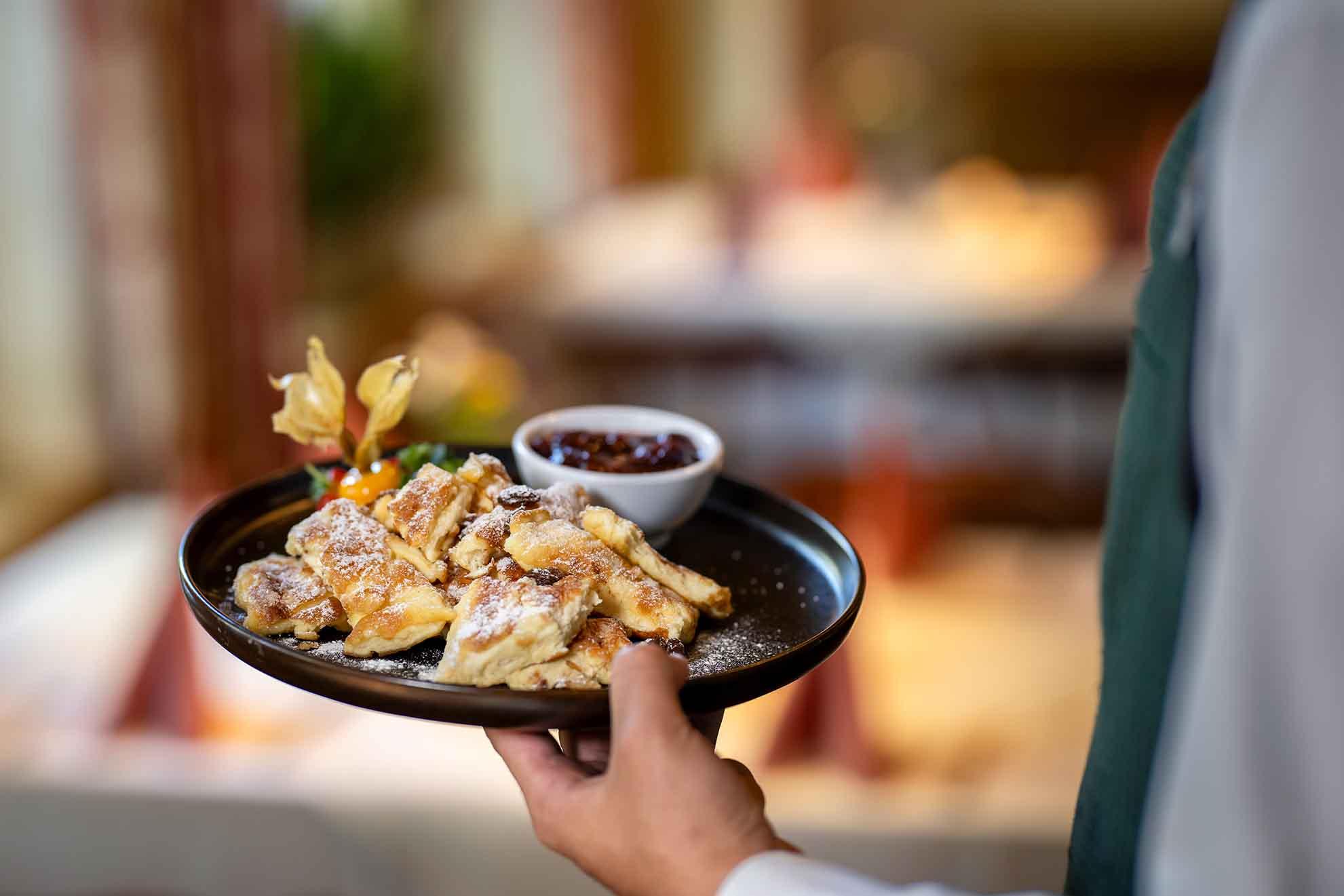 A plate with freshly prepared dishes, served by a waiter. Alongside, there is a small bowl of jam and decorative fruits.