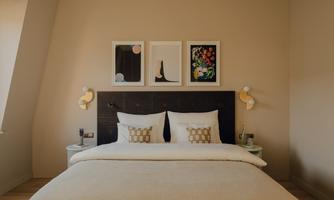 A cozy bedroom with a large bed and modern artwork on the wall. The colors are warm and inviting, perfect for relaxation.