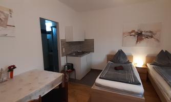 A simple room with two beds and a small kitchenette. The walls are painted light and there are decorative elements.