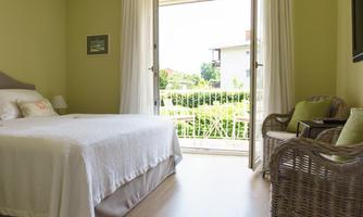 A cozy room with a double bed and soft green walls. Large windows provide a view of the garden outside.