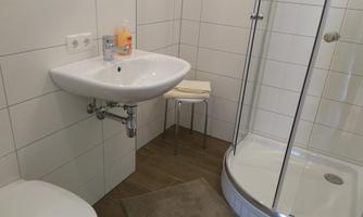 A modern bathroom with a shower and a sink. The walls are brightly tiled and there is a small chair.