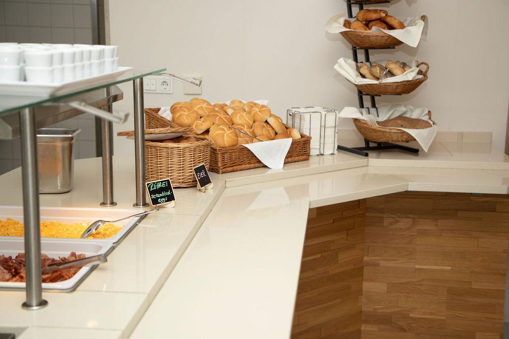 A buffet with various rolls and a selection of dishes. In the background, freshly baked breads are visible on a shelf.