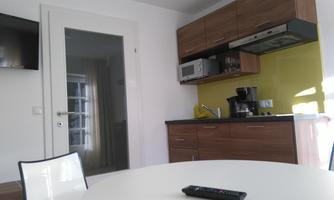 A modern kitchen with wooden cabinets and a bright yellow wall cabinet. There is a table with chairs and a television on the wall.