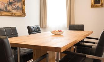 A modern conference table made of wood with black leather chairs. A bowl of fruit is on the table and the room is brightly lit.