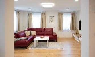 A modern living room with a red sofa and a white table. Large windows allow for plenty of daylight, and the wooden floor feels inviting.