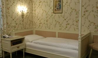A cozy bedroom with floral wallpaper pattern and a single bed. Next to the bed is a nightstand with a telephone.