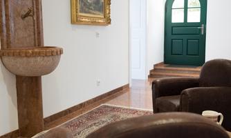 A stylish living room with an elegant table and cozy armchairs. In the background, there is a green door and a beautiful water fountain.