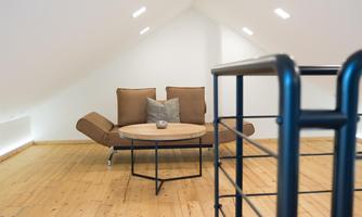 A modern living room in the attic with a brown sofa and a round table. The wooden floor and the light wall create a pleasant atmosphere.