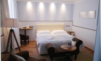 A cozy bedroom with a double bed and warm light. Next to the bed are a table and chairs, and a comfortable armchair invites you to relax.