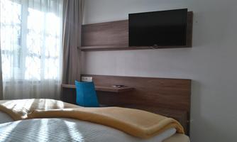 A simple room with a bed, a TV, and a desk. The window lets in a lot of daylight.