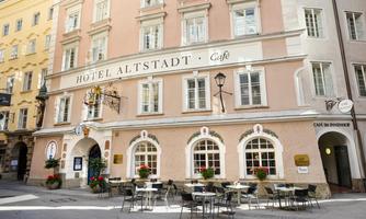A picturesque hotel building named "Hotel Altstadt" with an inviting café terrace. The facade is friendly and bright, surrounded by historic buildings.
