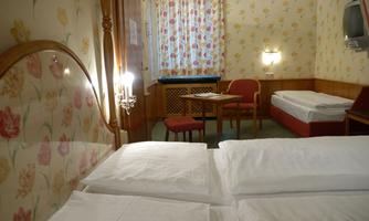 A cozy hotel room with two beds and a small table. The walls are decorated with floral wallpaper.