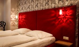A stylish bedroom with a red headboard and two soft pillows. The walls are decorated with an elegant pattern and indirect lighting creates a cozy atmosphere.