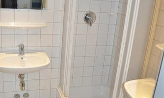 A modern bathroom with a shower, a sink, and large white tiles. A mirror is located on the wall above the sink.