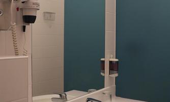 A modern bathroom with a round sink and a large mirror. The walls are painted in bright white and a soft blue.
