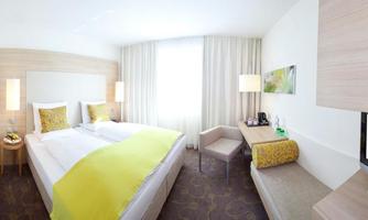 A modern hotel room with two beds and freshly decorated walls. Bright windows and elegant furniture create an inviting atmosphere.