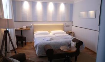 A modern bedroom with a large bed and soft colors. Next to the bed, there is a small table with a lamp and a chair.
