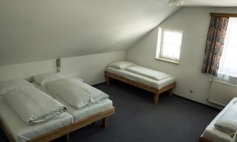 A simple bedroom with several beds and light walls. A window lets in daylight, and the floor is carpeted.