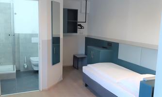A modern room with a single bed and a bathroom. The decor is simple and in light colors.