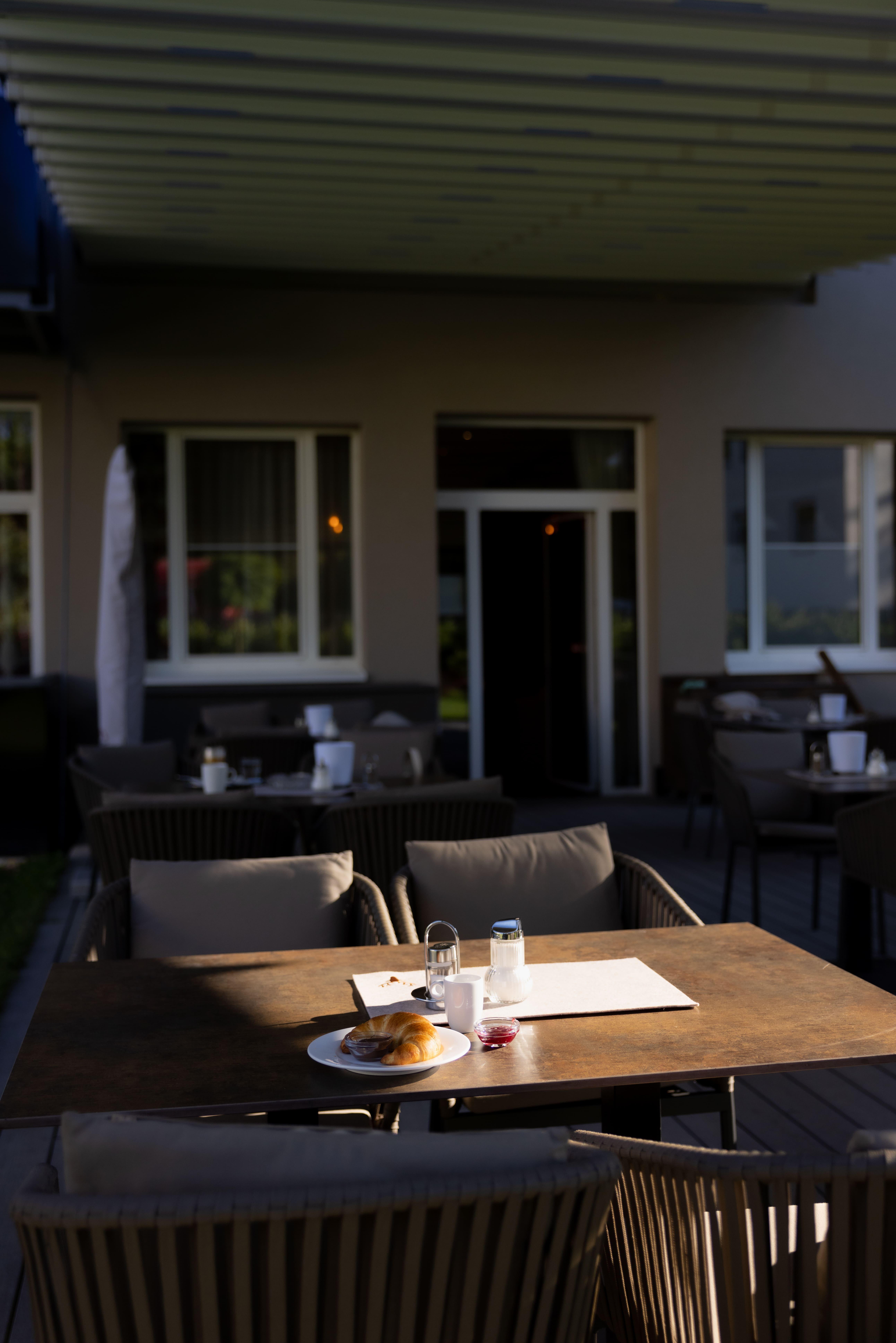 A beautiful outdoor area of a restaurant with tables and chairs. On a table, there is a pastry with a glass of water and a small bottle.