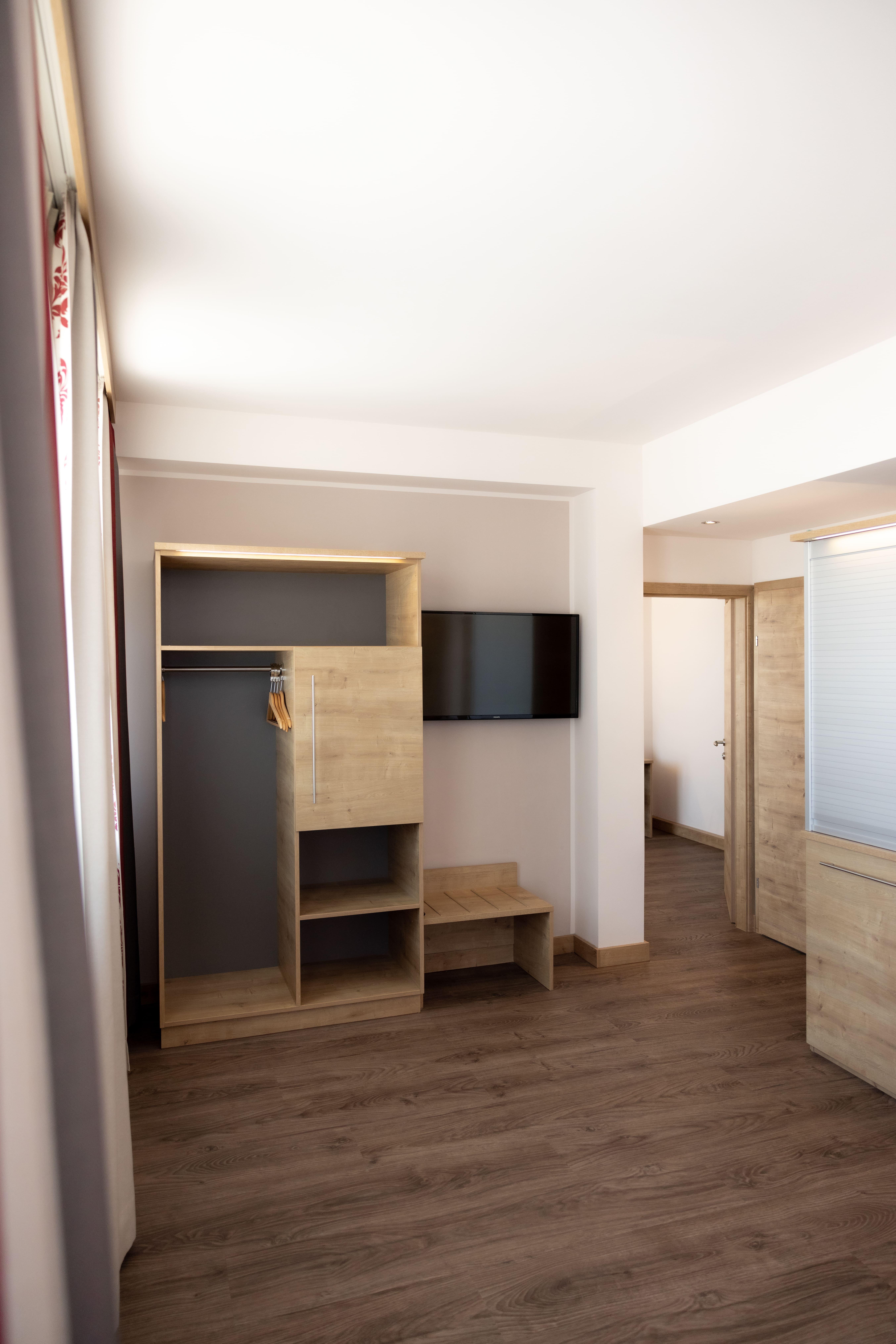 A modern room with wooden floors and bright walls. There is a wardrobe, a television, and a table.