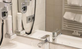 A modern bathroom with a sink, a towel rack, and a hair dryer on the wall. The decor is bright and designed in a minimalist style.