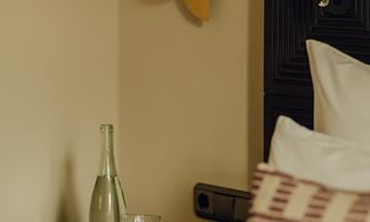 A stylish bedroom with a modern nightstand. On the table are a water bottle and a glass, next to a decorative light.